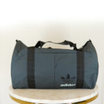 تصویر ساک ورزشی بغل جیب آدیداس طوسی با بند دوشی مشکی و آرم آدیداس مشکی با نوشته آدیداس سفید